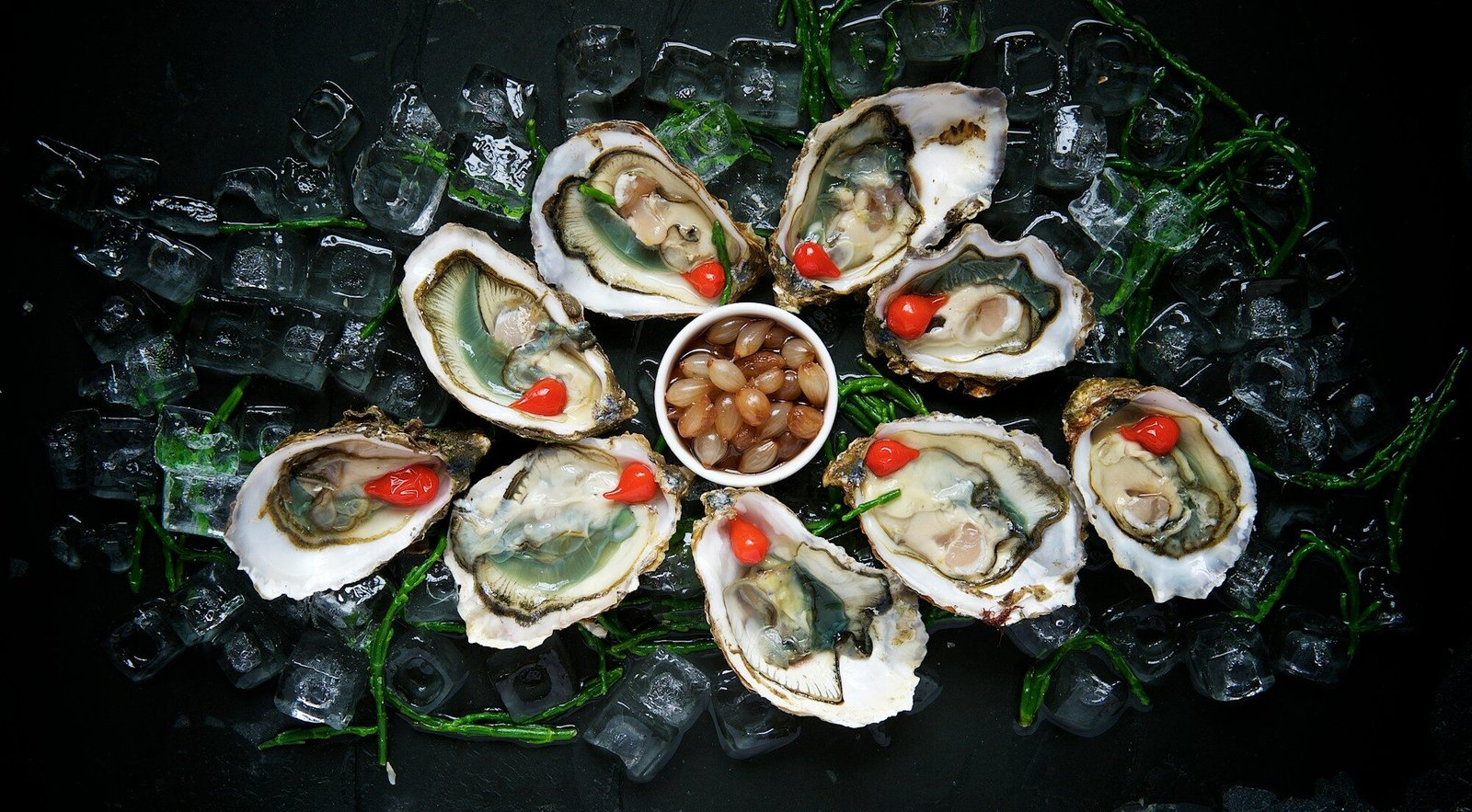 a plate of oysters on ice with a cherry in a bowl